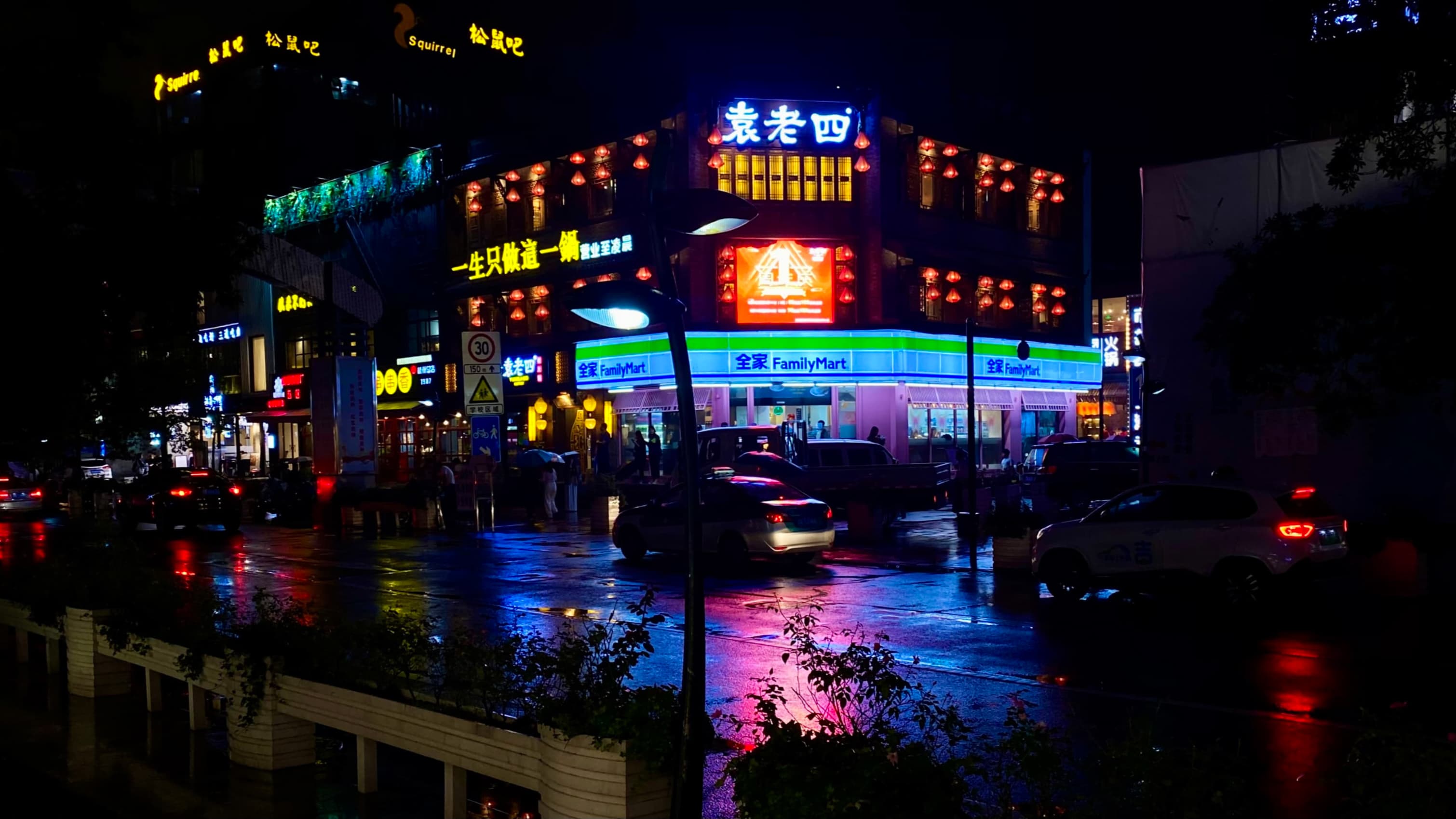 Intersection between Shihuqiao Road and Wulin Road on a rainy night, FamilyMart's neon lights reflected on the wet asphalt.